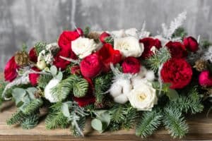 holiday centerpiece with red flowers white roses cottonflowers and greenery of pine, fir, and eucalyptus