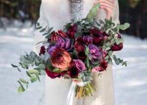 Winter bridal bouquet of dark burgundies and purples held by bride