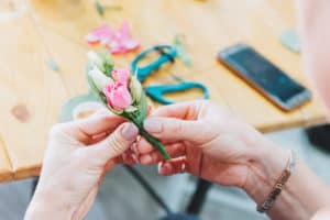Close up of hands of female caucasian florist as she is working on a groom's wedding boutonniere of white and pink roses