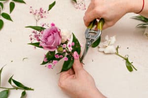 Process of making a boutonniere for the groom from cream and pink roses, ruskus leaves and pink gypsophila, top view