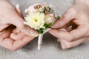 Florist at work. Steps of making wedding boutonniere with pink rose, ranunculus and white chrysanthemum.