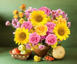 Still life with autumn flowers, sunflowers and roses, apples, rowan and gourd on artistic background