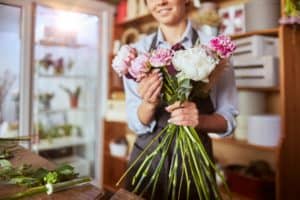 Portrait of female florist in apron arranging fresh flowers for bouquet in the flower shop, using roses, hydrangea, peonies. Small local business