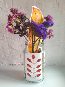 Glass jar with pink purple flowers on a white wall background. Interior decorating.
