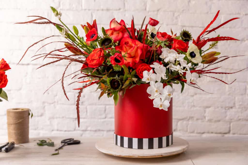 Red flowers arranged artfully in a modern red vase and white accent flowers