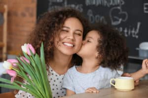 Kid kissing mom on the cheek and giving her flowers