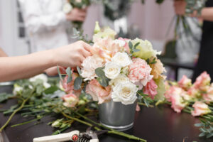 Hands working on pink and white bouquet in bucket