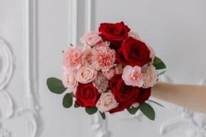 Hand holding bouquet of red roses and pink carnations