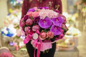 Woman holding paper wrapped bouquet of roses with orchids