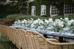 White florals and greenery on a long table outside near ivy covered walls