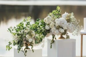Two white flower arrangements with greenery on pedestals