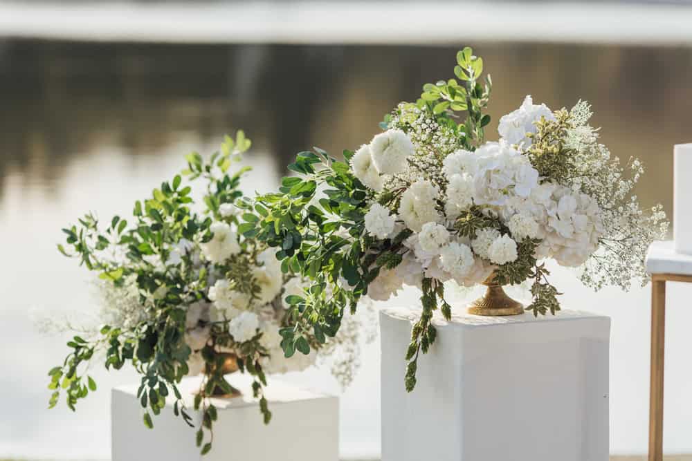 Two white flower arrangements with greenery on pedestals